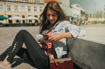 Young beautiful woman sitting in the city center holding a smartphone, smiling.