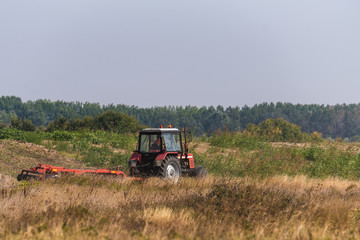 The red tractor works in the field in autumn