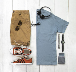 Fashionable concept, men’s clothes with sneakers, t shirt, yellow shorts, watch, sunglasses,sock, earphone and bracelet on white wooden background. pack shots, top view