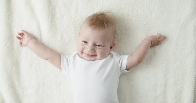 Little caucasian child happily smiling and laughing, lying on white bed sheet. happy childhood concept closeup 4k