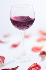 Red wine on a white background with rose petals