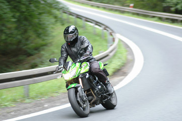 The driver of a green, sports motorcycle, wearing a complete safety suit, goes into a bend at high...