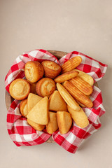 Wooden Bowl Lined with Red and White Checked Napkin Full of Cornbread Muffins, Sticks and Slices on Neutral Background