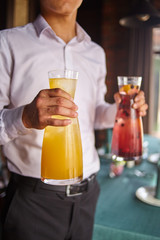 A young man or a waiter holds in the mouths decanters with fruit drinks
