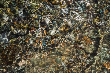 Varicolored detailed texture of stony bottom of transparent brook close up. Clean water in mountain creek. Colorful background of smooth stones in river stream with copy space.