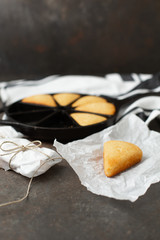 Slice on Homemade Cornbread Isolated on White Parchment Paper; Some Slices Wrapped in Parchment; Cast Iron Skillet with Cornbread in Background; Black Background