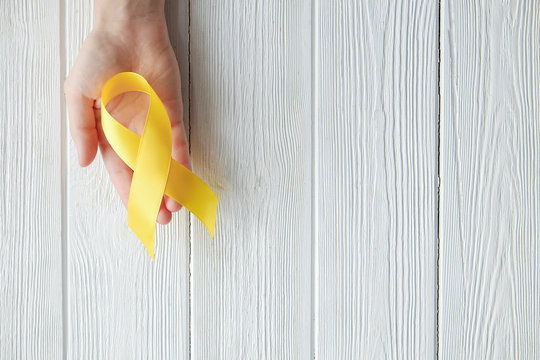 Woman's hand holding yellow ribbon - bladder, liver and bone cancer awareness symbol. Children cancer prevention concept. Isolated background, copy space, close up, top view