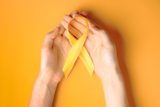 Woman's hand holding yellow ribbon - bladder, liver and bone cancer awareness symbol. Children cancer prevention concept. Isolated background, copy space, close up, top view