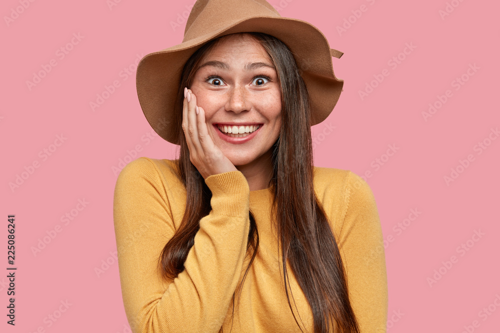 Wall mural portrait of happy overjoyed girl with appealing appearance, gazes with broad smile, has fun, dressed