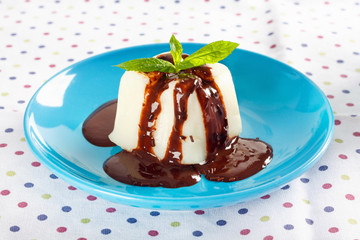 Cream pudding with chocolate sauce and mint on  multicolored tablecloth.