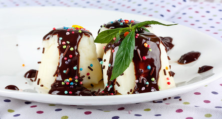Cream pudding with chocolate sauce, mint and cinnamon on  multicolored tablecloth.
