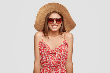 Photo of glad smiling young European woman traveler grins at camera has broad smile, wears summer fashionable outfit, poses against white background. Positive emotions and recreation concept