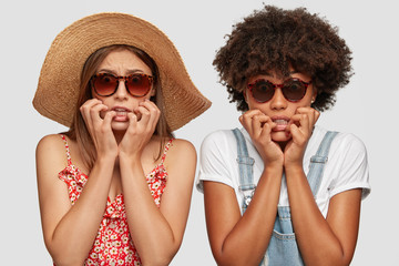 Scared nervous diverse women bite finger nails nervously, look desperately at camera, stand next to...