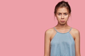Offended Caucasian girl with insulted expression, scowls face, puses lips in discontent, has...