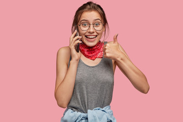 Indoor shot of cheerful Caucasian woman shows okay gesture, keeps thumb raised, expresses her...