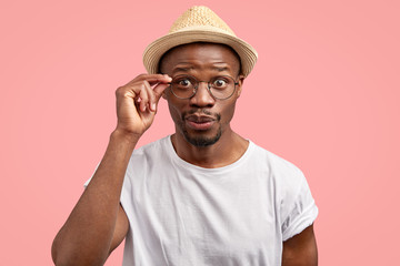 Photo of curious African American male looks with mysterious expression, keeps hand on rim of...
