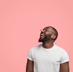 Vertical shot of cheerful dark skinned unshaven man looks positively upwards, being in good mood,...