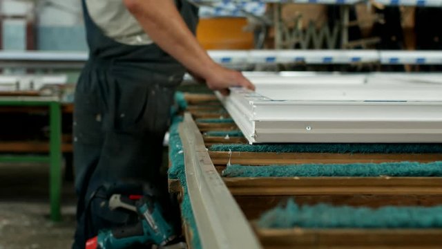 Production and manufacturing of pvc windows, a male worker assembles a pvc profile window, drills a hole in the pvc profile for mounting hinged parts, drill window