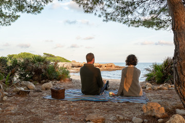 Pareja, hombre y mujer, haciendo un picnic otoñal en una playa mediterránea al atardecer.