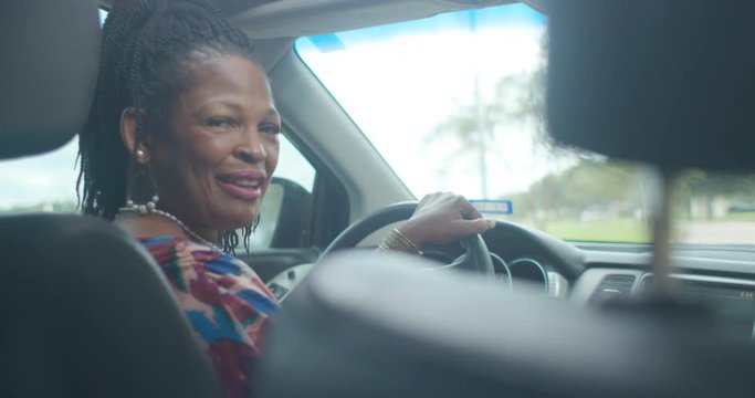 Friendly African American ride sharing driver looks over her shoulder to talk to her customer.