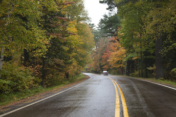 Car driving on a curving road in northern Minnesota with trees in autumn color on a rainy day