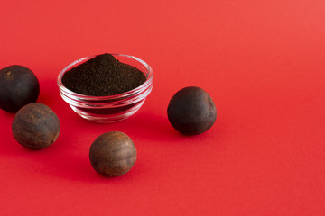 Black lemon powder in a glass bowl, whole dried black lemons on the red background. Copy space.