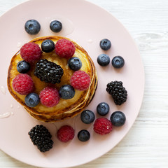 Pancakes with berries and honey on a pink plate on white wooden backfround, overhead view. Close-up.