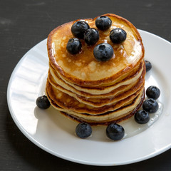Pancakes with blueberries and honey on white round plate on dark wooden background, side view. Close-up.