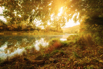 Beautiful sunny autumn landscape with reflection in the water and sun shine