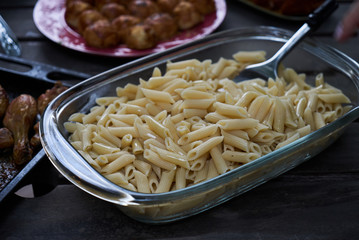 Party snack food table with baked potatoes, fried chicken drumsticks, italian pasta and puff pastry buns bread, close-up. Table with variety food top view. 