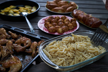 Party snack food table with baked potatoes, fried chicken drumsticks, italian pasta and puff pastry buns bread, close-up. Table with variety food top view. 