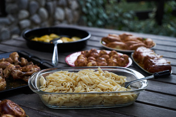 Party snack food table with baked potatoes, fried chicken drumsticks, italian pasta and puff pastry buns bread, close-up. Table with variety food top view. 