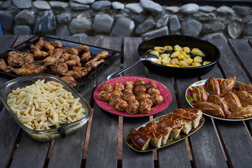 Party snack food table with baked potatoes, fried chicken drumsticks, italian pasta and puff pastry buns bread, close-up. Table with variety food top view. 