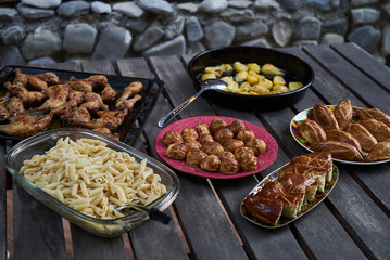 Party snack food table with baked potatoes, fried chicken drumsticks, italian pasta and puff pastry buns bread, close-up. Table with variety food top view. 