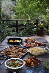 Party snack food table with baked potatoes, fried chicken drumsticks, italian pasta and puff pastry buns bread, close-up. Table with variety food top view. 