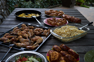 Party snack food table with baked potatoes, fried chicken drumsticks, italian pasta and puff pastry buns bread, close-up. Table with variety food top view. 