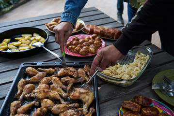 Catering buffet food table with baked potatoes, fried chicken legs, pasta and vegetable salad. People at a party taking different food, outdoor. Colleagues Buffet Party Brunch Dining Concept
