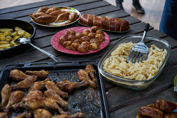 Catering buffet food table with baked potatoes, fried chicken legs, pasta and vegetable salad. People at a party taking different food, outdoor. Colleagues Buffet Party Brunch Dining Concept