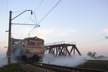 Early in the morning, when the street is foggy, the train is riding on the railway bridge