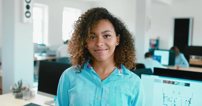 Portrait of young adult mid beautiful African American black female smiling and looking into camera, busy office in the background. 4K UHD 60 FPS SLOW MOTION