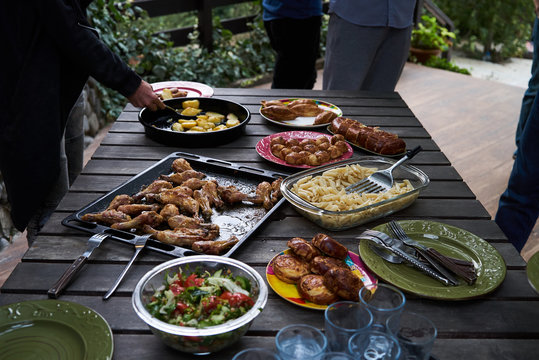 Catering Buffet Food Table With Baked Potatoes, Fried Chicken Legs, Pasta And Vegetable Salad. People At A Party Taking Different Food, Outdoor. Colleagues Buffet Party Brunch Dining Concept