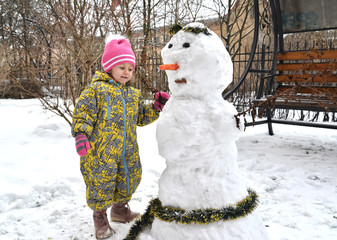 The little girl plays with a snowman