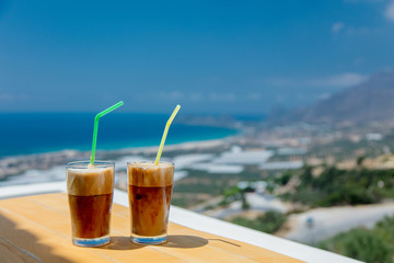 Two little glasses with cold cappuccino and tubule on a wooden table in Greece cafe in summertime
