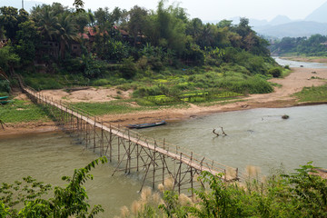 Fototapeta na wymiar View of a bamboo bridge over Nam Khan River at low tide and lush riverbank in Luang Prabang, Laos, on a sunny day.