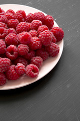 Raspberry on a pink plate on black background, close-up.