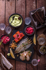 Assorted marinated fish on dark cutting board with vodka shots.