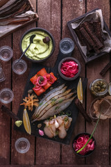 Assorted marinated fish on dark cutting board with vodka shots.