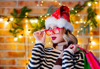 Portrait of a young cozy woman with shopping bags and Christmas lights and pine branch on background.