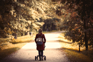 Young woman strolling in a park with stroller and a child in autumn season