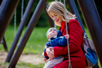 Obraz premium Young mother and a child on children's swing at playground in a park